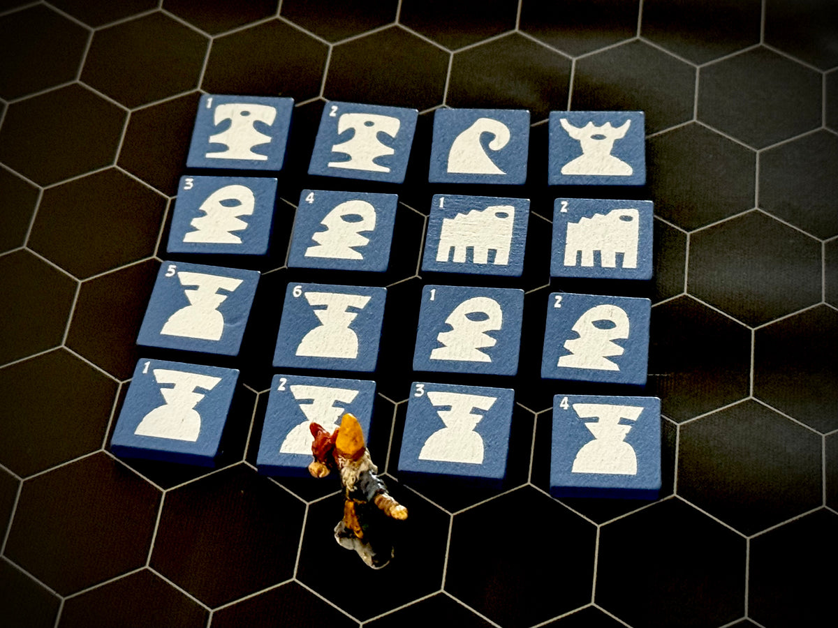 Blue QuoDrox tiles showing the front designs on a black hex map.  A miniature figure stands in the front. 